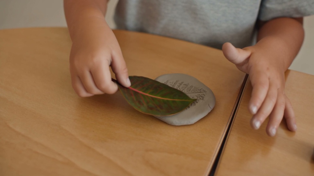 A child pressing a gum leaf into a flat disc of clay on the studio table